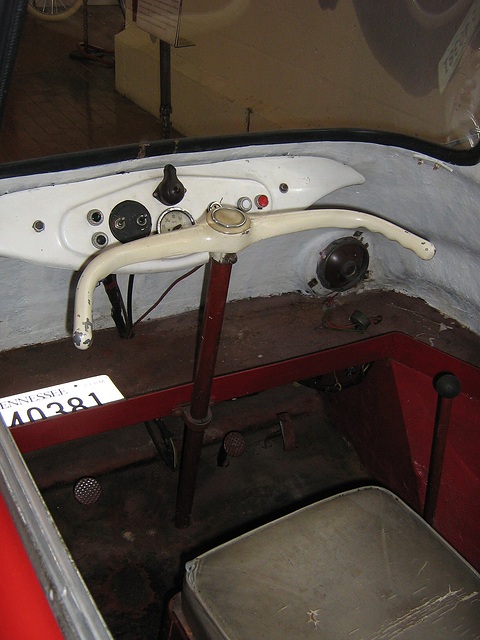 Cream handlebar and small dials inside a red cabin, a bare seat box below. Opens a larger view