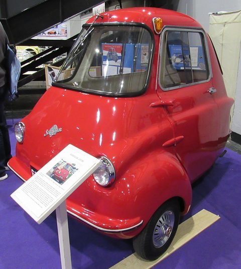 Red three-wheeler on a purple carpet with an information board in front of it. Opens a larger view