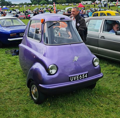 Purple three-wheeler on grass seen from the front left, a man standing behind it. Opens a larger view