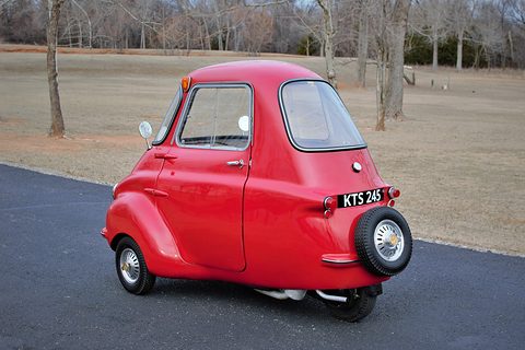 Red three-wheeler seen from the rear right with a spare wheel mounted on its back. Opens a larger view