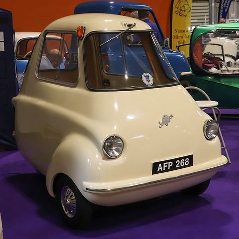 Cream three-wheeler on a purple carpet, seen from the front right. Opens a larger view