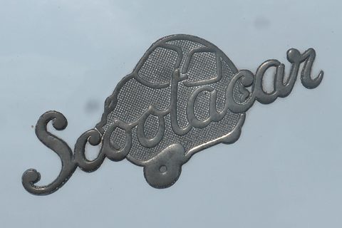 Chrome Scootacar script over a textured car-shaped plaque on grey paint. Opens a larger view