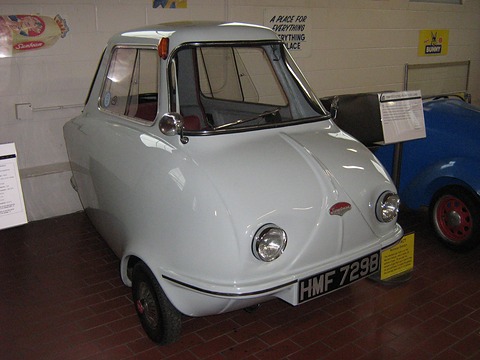 Pale grey three-wheeler with a separate bonnet and twin headlamps on a brick floor