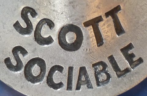 Close view of a worn aluminium plate with the raised words Scott Sociable curving round its face. Opens a larger view