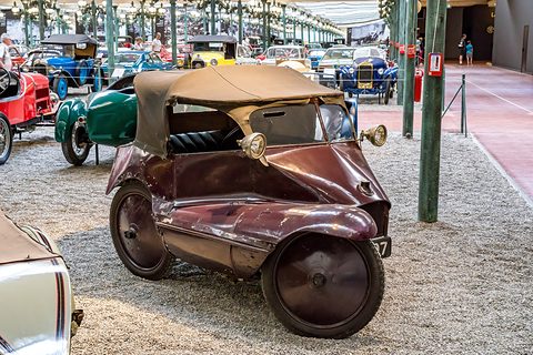 A maroon three-wheeler with a tan hood seen from the offside, its two rear wheels and brass lamps visible. Opens a larger view
