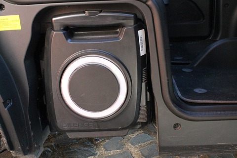 Black wheeled battery case with a round white handle ring standing in a bay inside an open car door. Opens a larger view