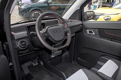 Black dashboard and two-spoke steering wheel, door trim with red stitching and grey fabric seats. Opens a larger view