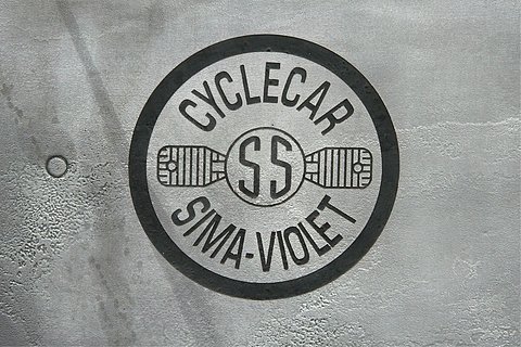A circular badge with a flat-twin engine drawing between the words Cyclecar and Sima-Violet on dull metal. Opens a larger view
