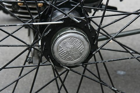 A cast aluminium hub cap with raised lettering at the centre of a black-spoked wire wheel. Opens a larger view