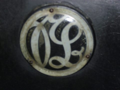 A round nickel badge with an interlaced S and B monogram on black bodywork. Opens a larger view