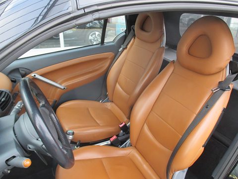 Two tan leather bucket seats, a black steering wheel and tan door trim seen through the open driver’s door. Opens a larger view
