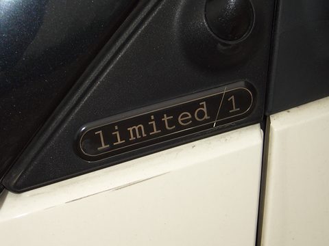 Close view of an oval black and silver badge reading limited/1 on a black pillar above a cream door. Opens a larger view
