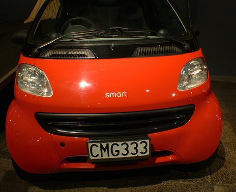 Front of a red two-seater with a black grille, smart lettering and a CMG333 plate against a dark background. Opens a larger view