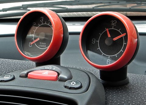 Two red-rimmed round dials, a rev counter and a clock, on stalks above a hazard switch and dashboard. Opens a larger view