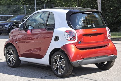 Rear of a red electric two-seater with a white safety cell and large tail lamps in a car park. Opens a larger view