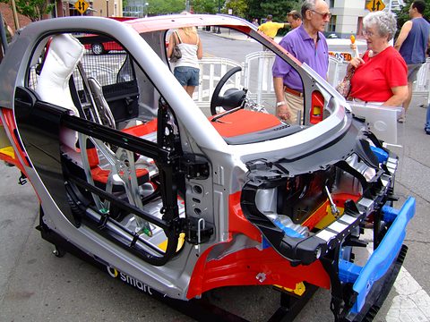 Sectioned silver and red car body with seats, steering wheel and engine exposed, visitors looking on.