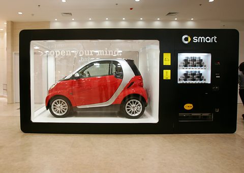 Red and silver two-seater inside a huge black vending-machine display case in a shopping mall. Opens a larger view
