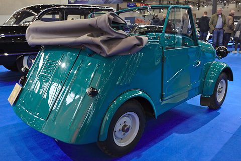 Rear quarter of a teal microcar with louvres on its sloping tail and a grey hood folded over the back. Opens a larger view