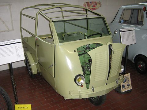 Pale green three-wheeled van with its bonnet open over the front-wheel engine, an open tubular cab frame and a flat load bed.
