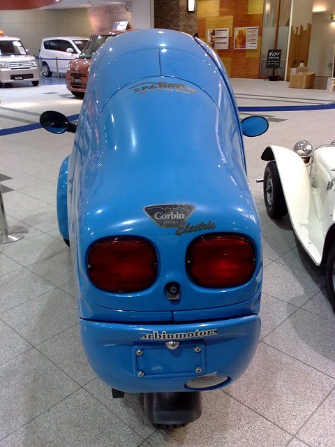 Tail of a blue three-wheeler with two large round red lamps, a Corbin badge and its single rear wheel. Opens a larger view