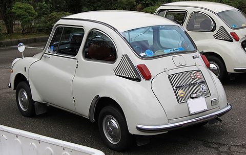 Rear three-quarter of a white small car with a vertical-slatted engine lid, club badges and side air intakes. Opens a larger view