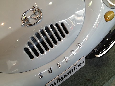 Close view of a chrome six-star badge above a row of vertical slots and spaced chrome letters on a pale grey nose. Opens a larger view