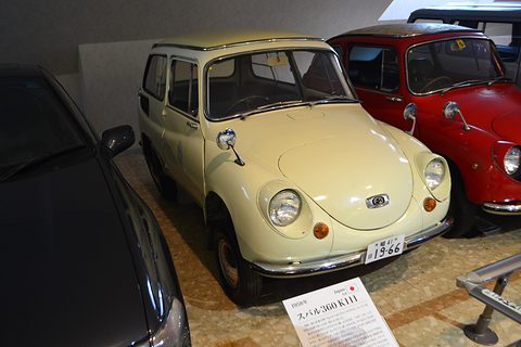 Cream small estate car with a rounded nose and flat roof, parked between a red Subaru 360 and a dark modern car. Opens a larger view