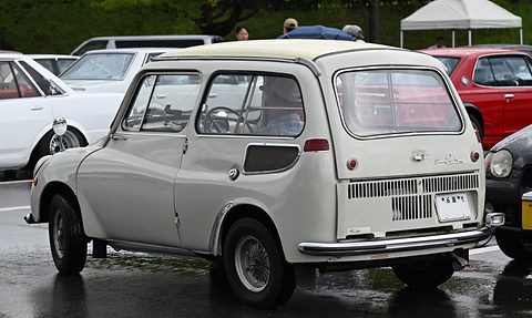 Rear three-quarter of a pale grey small estate with a lift-up tailgate, slatted lower panel and chrome bumper, on wet tarmac. Opens a larger view
