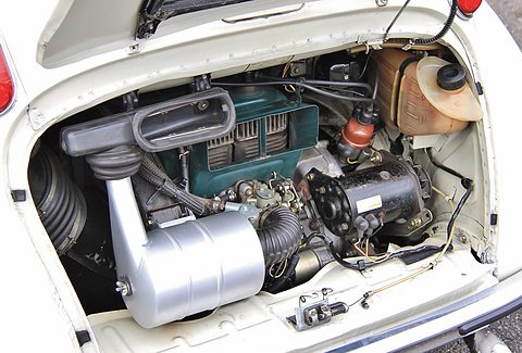 Open rear engine lid showing a green finned engine, silver air cleaner, cooling hoses and a plastic oil tank.