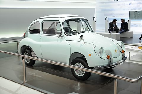 Pale green rounded small saloon with front-hinged doors and chrome trim behind a steel rail on a dark stand. Opens a larger view