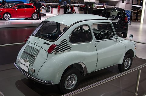 Rear three-quarter of a pale green small car with vertical louvres on the engine lid and side air intakes. Opens a larger view