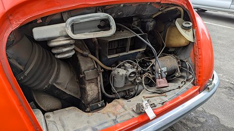 Open rear engine compartment with a dusty engine, carburettor, cooling hose and a yellowed oil tank. Opens a larger view