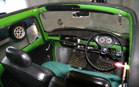 Looking into a green open car: black seats, a black steering wheel and two round dials in a black binnacle. Opens a larger view