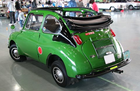 Rear three-quarter of a green small car with its fabric roof folded at the back and a slatted engine lid. Opens a larger view