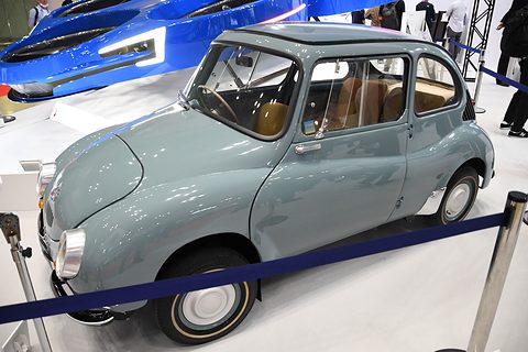 Side view of a grey-blue small fastback saloon with white-wall tyres behind a blue rope barrier.