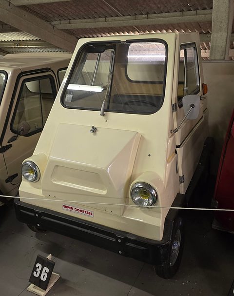 Cream boxy four-wheeled microcar with Super Comtesse lettering on the nose, behind a rope with a number board. Opens a larger view