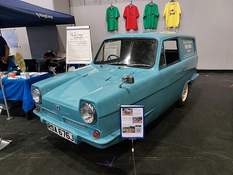 Pale blue three-wheeled van on a club stand, coloured T-shirts hanging on the wall behind.