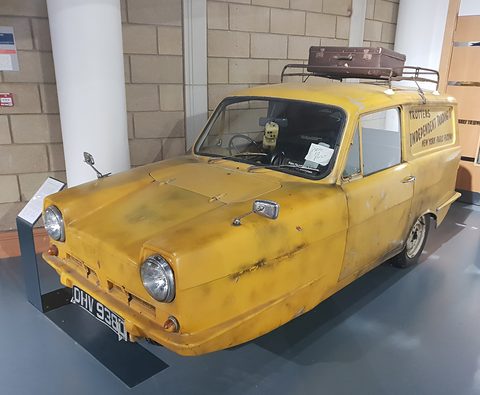 Grimy yellow three-wheeled van with a suitcase on its roof rack and a Tax in Post note in the windscreen.