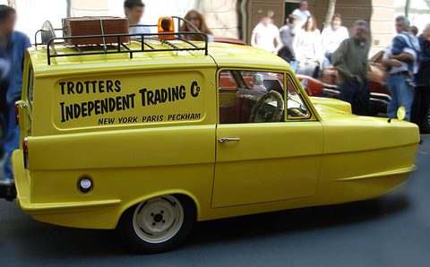 Yellow van with a suitcase and orange beacon on its roof, onlookers crowding behind. Opens a larger view