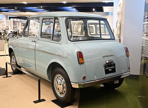 Rear three-quarter of a pale blue small saloon with a rear window, round tail lamps and a black display plate. Opens a larger view