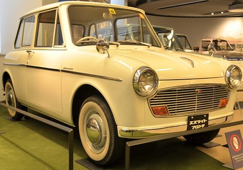 Cream small two-door saloon with a horizontal-bar grille, round headlamps, fender mirrors and white-wall tyres. Opens a larger view