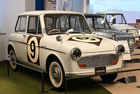 Cream small saloon with a large black number 9 on white roundels on its door and bonnet, behind a low rail. Opens a larger view