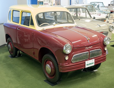 Maroon and cream small van with round headlamps and a split chrome grille on green carpet, other old cars behind. Opens a larger view