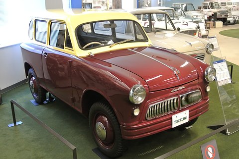 Small two-tone van with a maroon lower body, a yellow upper body and side windows, barred grille, on green carpet. Opens a larger view