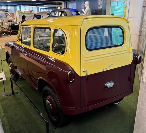Rear three-quarter of a maroon and yellow van with a large rear window in a side-hinged tailgate door. Opens a larger view