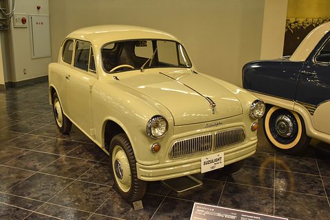 Cream small two-door car with a split chrome grille and round headlamps on a polished dark floor.