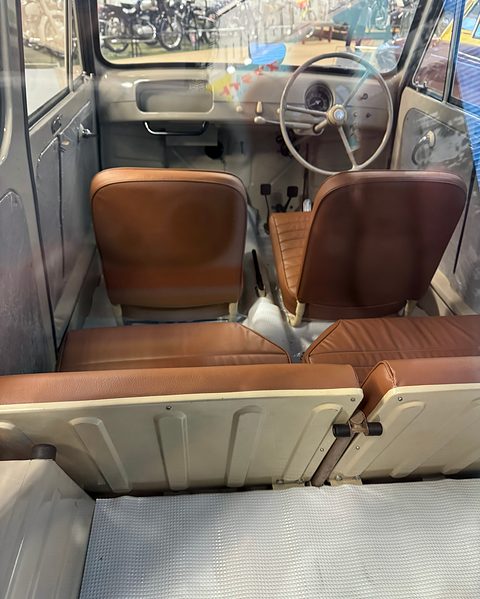 View from the back of a small van: a ribbed load floor, a folded rear bench, two brown seats and a cream steering wheel. Opens a larger view