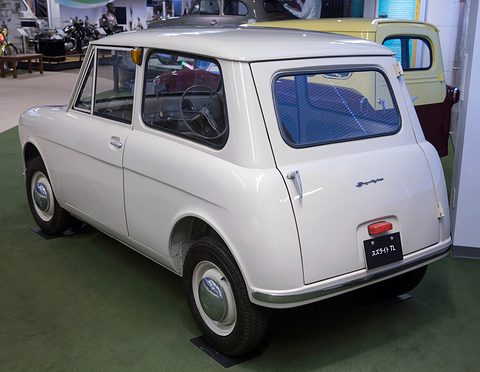 Rear view of a cream boxy small van with a large rear window, a single tail lamp and a black plate. Opens a larger view