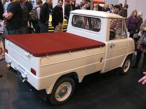 Rear three-quarter of a cream pickup with a maroon tonneau cover, a crowd of show visitors behind. Opens a larger view