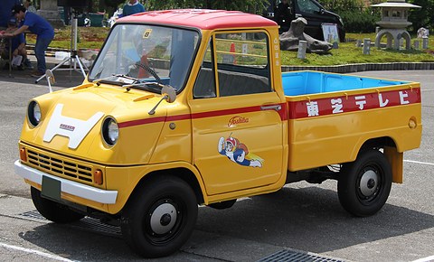 Yellow pickup with a red roof, a white H badge on the nose and red Japanese lettering along the bed sides. Opens a larger view